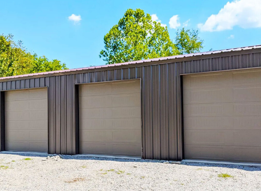 a row of tan commercial garage doors on a building with trees in the background